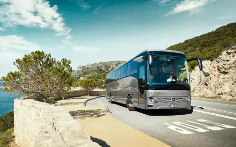 Srebrny Mercedes Tourismo jedzie malowniczą trasą nad morzem.