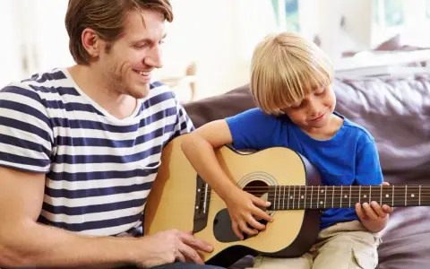 Ojciec uczy syna grać na gitarze. Radosna szkoła gry na gitarze w domowym zaciszu.
