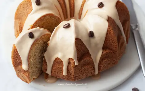 Deliziosa torta al caffè con glassa chiara e chicchi di caffè come decorazione. Una fetta è stata tagliata, mostrando la morbida consistenza interna.