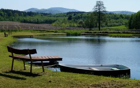 Idealne miejsce na camping nad stawami: łódka przy pomoście, ławka i spokojna tafla wody.