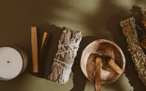 Palo santo kadzidło właściwości: świeca, biała szałwia, miseczka z drewienkami palo santo i bukiety ziół.