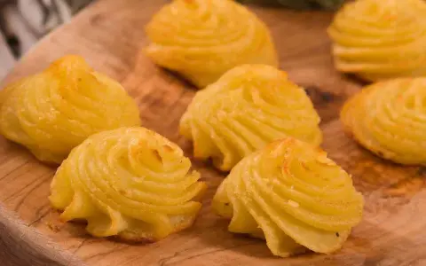 Patate duchessa dorate e invitanti, disposte su un tagliere di legno, pronte per essere gustate.