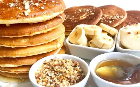 Pile de pancakes dorés arrosés de miel, accompagnés de rondelles de banane, de noix concassées et d'une cuillère de miel. Un délice pour le petit-déjeuner !