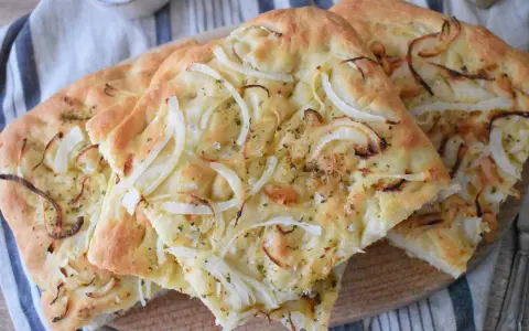 Pyszna focaccia z cebulą, posypana ziołami i solą, prezentuje się apetycznie na drewnianej desce.