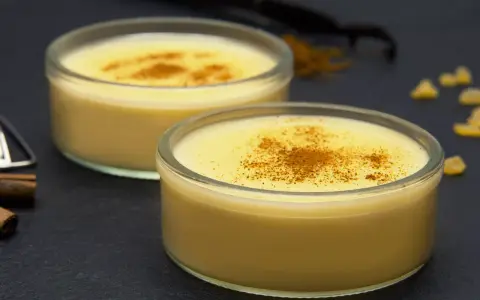Dos cuencos de natillas caseras, espolvoreadas con canela, junto a palitos de canela y vainilla.