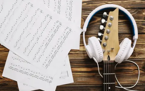 Nuty i gitara z białymi słuchawkami. Idealne do tego, by znaleźć piosenkę po nuceniu i stworzyć własną melodię.