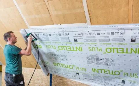 Mann bringt mit einem Tacker eine Dampfbremse an. Die Folie ist mit "INTELLO PLUS" bedruckt.