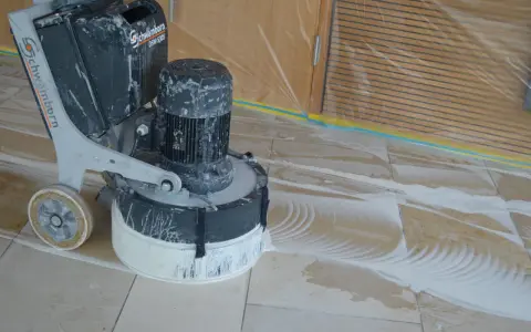 Bodenmaschine poliert Marmor. Staub und Wasser bilden Muster auf dem Boden, während die Maschine den Stein glänzend macht.