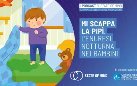 Bambino triste nel letto con macchia sul pigiama, affronta l'enuresi notturna. Un orsacchiotto conforta.