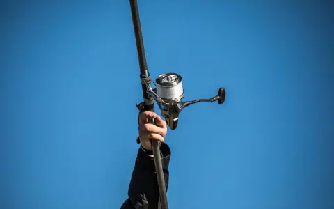 Ręka trzyma wędkę z kołowrotkiem, gotowa do wiązania żyłki na kołowrotek.