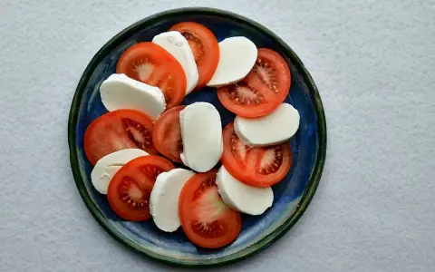 Plasterka pomidorów i mozzarelli ułożone naprzemiennie na niebieskim talerzu.