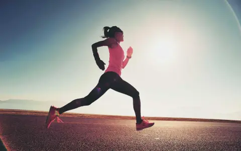 Donna corre su strada asfaltata al tramonto, con il sole che illumina la scena. Questo è un esempio di tempo run, un allenamento per migliorare la velocità.
