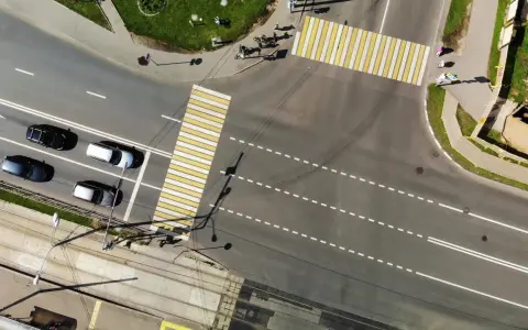 Vista aerea di un incrocio con strisce pedonali bianche e gialle. Auto in attesa nella corsia di preselezione, tram sui binari sottostanti.