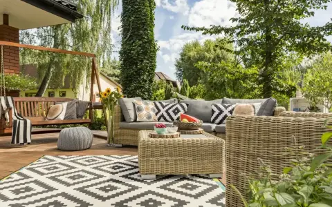 Relaks na tarasie w stylu boho: wiklinowe meble, huśtawka, wzorzysty dywan i mnóstwo zieleni.