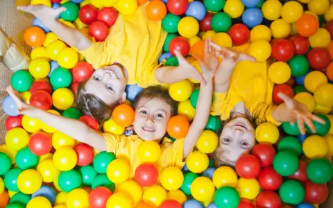 Drei Kinder in gelben T-Shirts spielen in einem Bällebad. Perfekte Ausflugsziele mit Kindern für Spaß und Lachen.