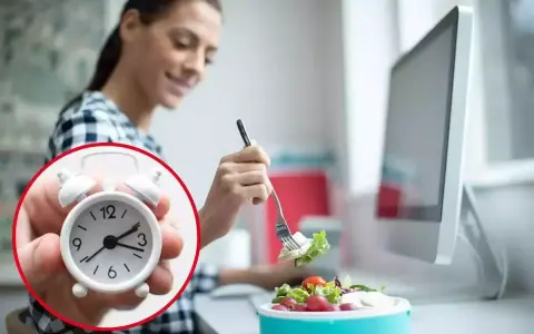 Mujer comiendo ensalada en su escritorio, con un reloj que marca el tiempo para comer en el trabajo.