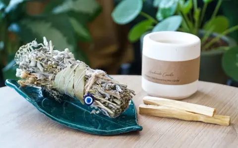 Ziołowe kadzidło na zielonej podstawce, obok świeca i patyczki palo santo. Idealne do rytuału, jak zrobić kadzidło.