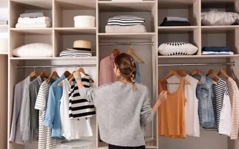 Kobieta porządkuje szafę, wieszając ubrania. Widać półki z poukładanymi rzeczami i wieszaki z odzieżą. To inspiracja, wie organisiert man den kleiderschrank.