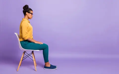 Donna seduta su una sedia, con le mani appoggiate sulle ginocchia, in una posa che suggerisce le **tecniche di grounding** per ritrovare la calma.