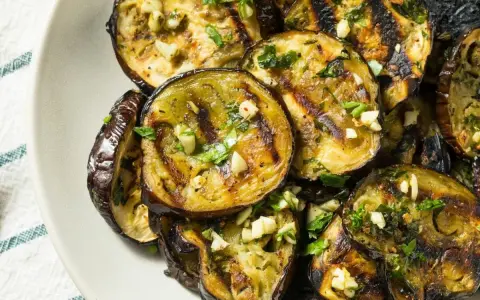Aubergines grillées en rondelles, garnies d'ail et de persil, sur une assiette.