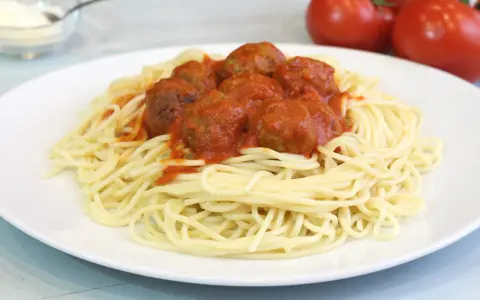 Un plato de espaguetis con albóndigas cubiertos de salsa roja.