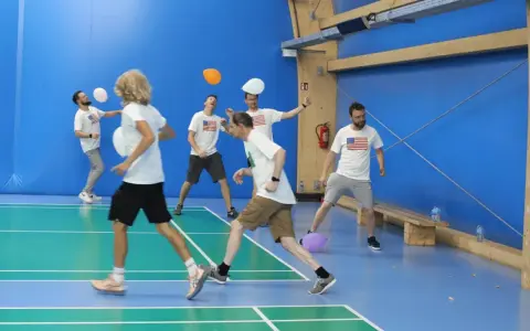 Mężczyźni w koszulkach z amerykańską flagą grają w gry zespołowe dla dorosłych, odbijając balony na hali sportowej.