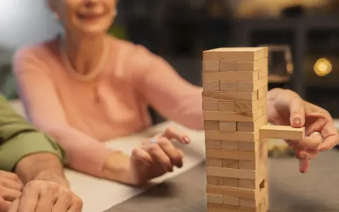 Uśmiechnięta seniorka wyciąga klocek z wieży Jenga. Wspaniałe konkursy zabawy dla seniorów!