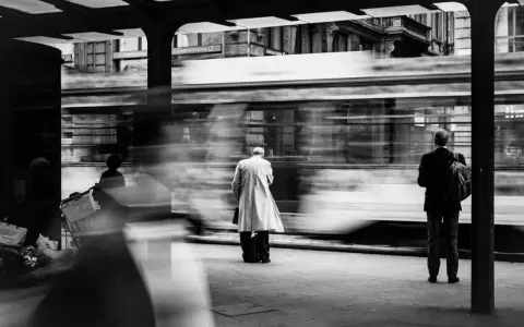 Street photography esempi: un tram sfreccia, lasciando figure sfocate in attesa alla fermata.