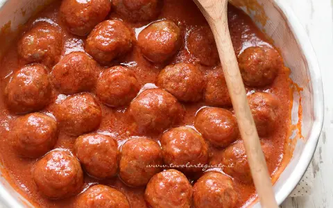 Polpette al sugo fumanti in una ciotola, pronte per essere gustate. Un cucchiaio di legno le accompagna.