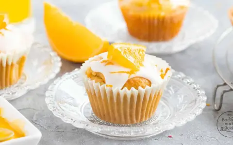 Fanta Muffins mit weißer Glasur und Orangenspalten, serviert auf kleinen Glastellern.