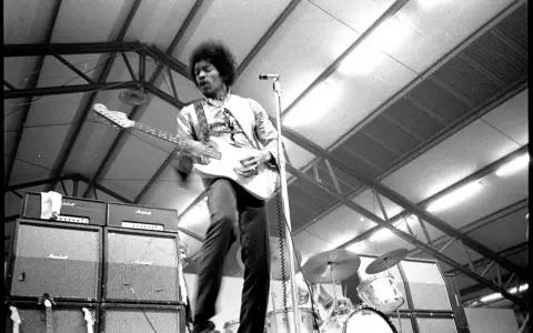 Jimi Hendrix, icône du jimi hendrix style de musique, électrise la scène avec sa guitare blanche. Amplis Marshall et batterie en arrière-plan.