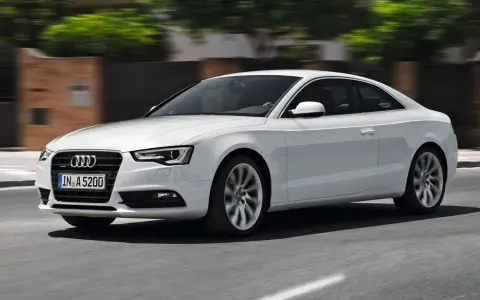Białe Audi A5 Coupe pędzi po drodze, jego sylwetka jest dynamiczna i elegancka.