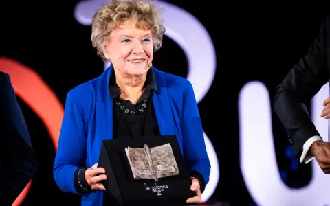 Una donna sorride sul palco, tenendo un premio a forma di libro aperto. Un simbolo di ispirazione per le libere donne.