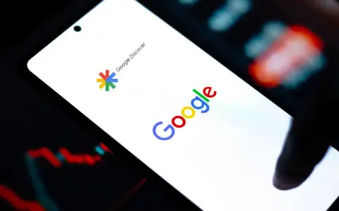 Ekran smartfona z logo Google i napisem Google Discover. W tle wykresy giełdowe.