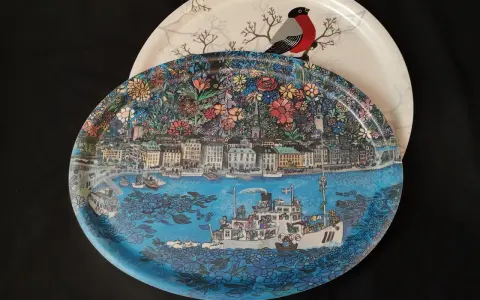Två brickor, en med en detaljerad stadsvy och fartyg, den andra med en domherre och träd. En fin bengt elde bricka.