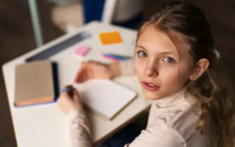 Dziewczynka zmagająca się z dysleksją rozwojową próbuje pisać w zeszycie, patrząc z nadzieją na pomoc.