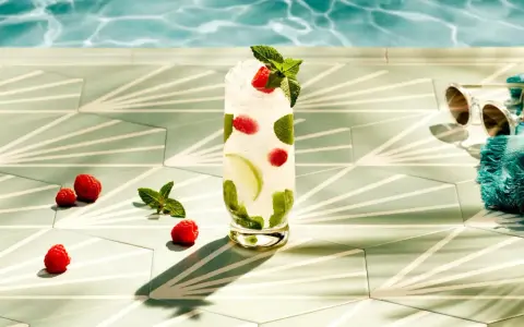 Orzeźwiający drink z malinami i miętą, idealny do Bacardi malinowego. Obok leżą maliny, a w tle widać basen i okulary przeciwsłoneczne.