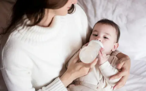 Mama karmi butelką dziecko, które właśnie pije mleko. Ważne jest, ile mleka powinien jeść noworodek.