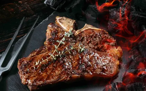 Un jugoso chuleton a la brasa, con romero fresco, listo para ser servido junto a brasas ardientes.
