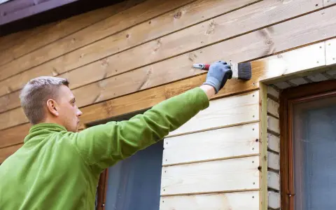 Mężczyzna maluje deskę elewacyjną, tworząc piękne aranżacje. Drewno nabiera nowego blasku.