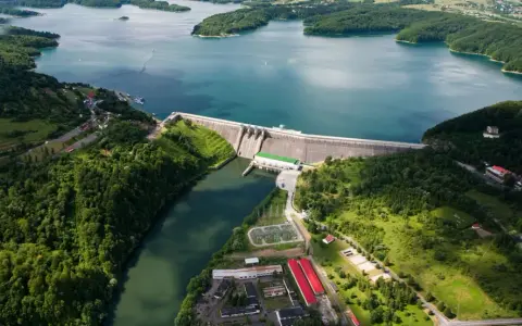 Zapora Solina z lotu ptaka, otoczona zielonymi wzgórzami i błękitną wodą. Planujesz wycieczkę? Sprawdź zapora Solina bilety!