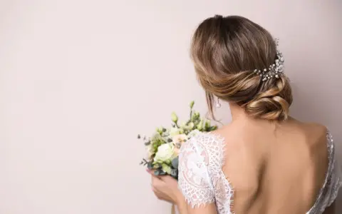 Eleganckie wesele: wlosy podpiete z jednej strony, ozdobione perłami, z bukietem kwiatów w dłoni.