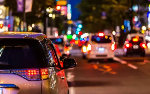 Luci sfocate e colorate in una strada trafficata di notte, come vedono i miopi le luci. Un'auto argentata in primo piano.