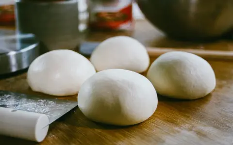 Cztery kulki ciasta na pizzę leżą na drewnianym blacie. Zastanawiasz się, jak rozmrozić ciasto na pizzę? To proste!