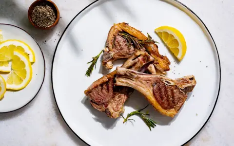 Côtelettes d'agneau grillées, parfumées à la marinade, garnies de romarin frais et de quartiers de citron.