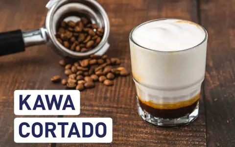 Kawa cortado z mleczną pianką, obok portafilter z ziarnami kawy. Idealny napój na poranek.