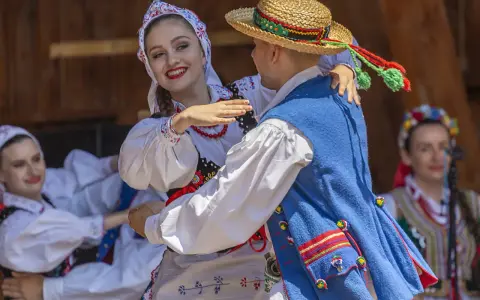 Uśmiechnięta para w tradycyjnych strojach tańczy do skocznych piosenek ludowych.