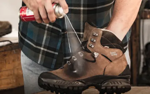 Jak zabezpieczyć nowe buty skórzane? Mężczyzna spryskuje brązowe buty trekkingowe preparatem ochronnym.