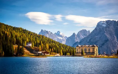 Lago alpino con hotel giallo e boschi autunnali, ideale tra i laghi da visitare in giornata.