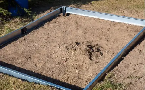 Metalowa rama na ziemi, gotowa na zrobienie fundamentu pod szklarnię.
